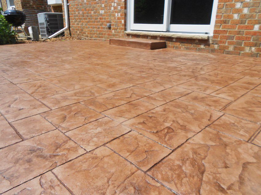Stamped concrete patio outside brick house with sliding glass door and small step