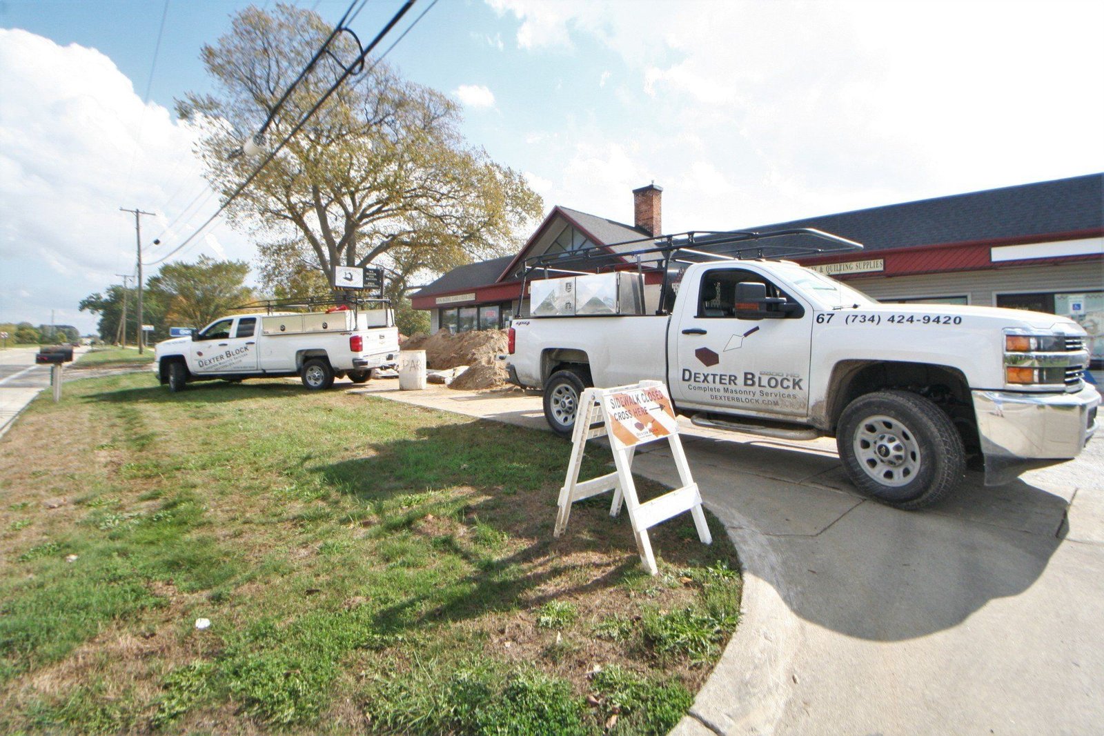 White utility trucks parked beside a house with a roadside barricade in front