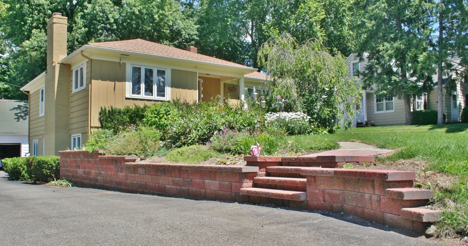 Yellow house with a raised brick planter wall and steps in a leafy residential yard