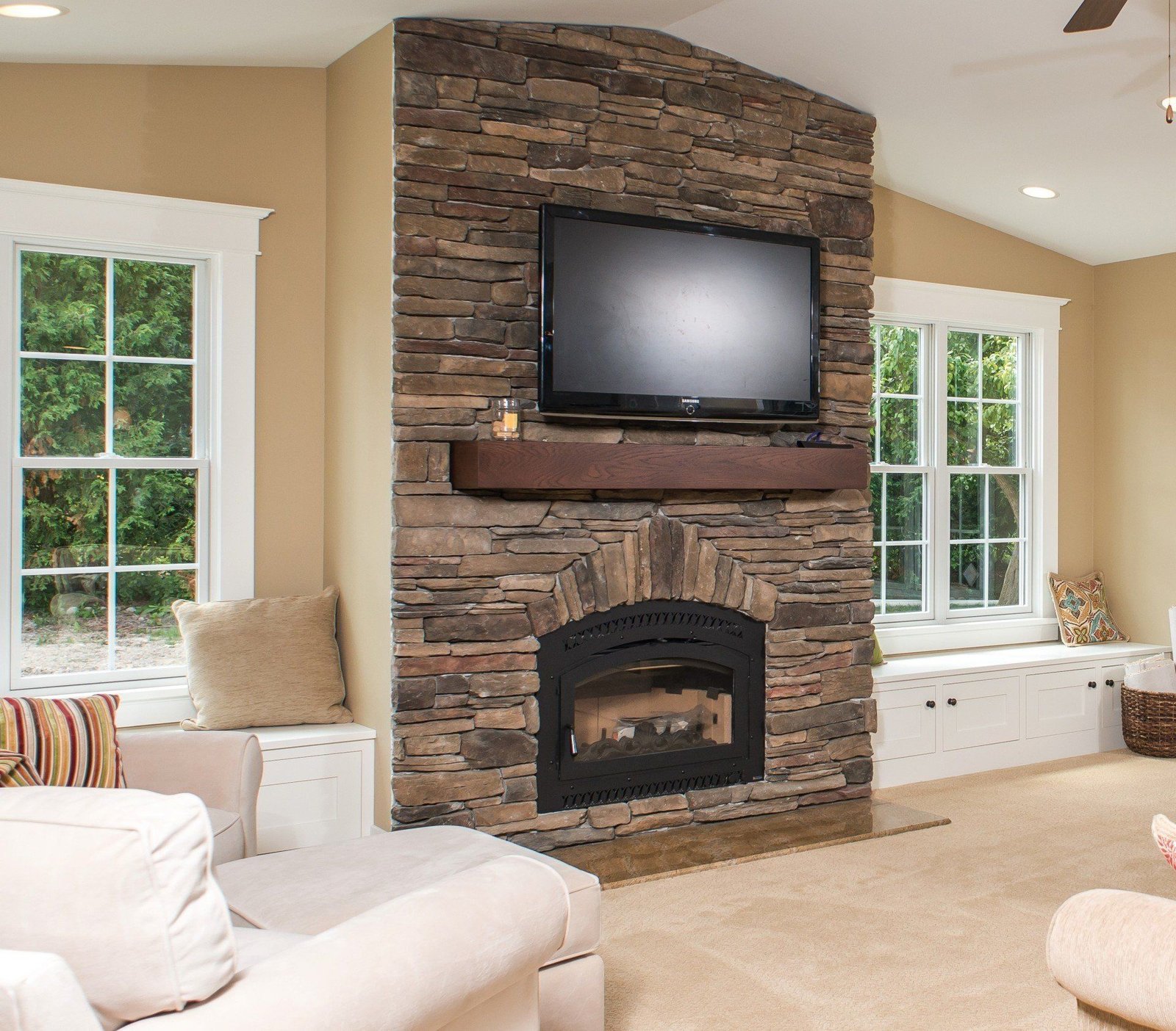 Living room with stone fireplace, mounted TV, and large windows with built-in white seating.