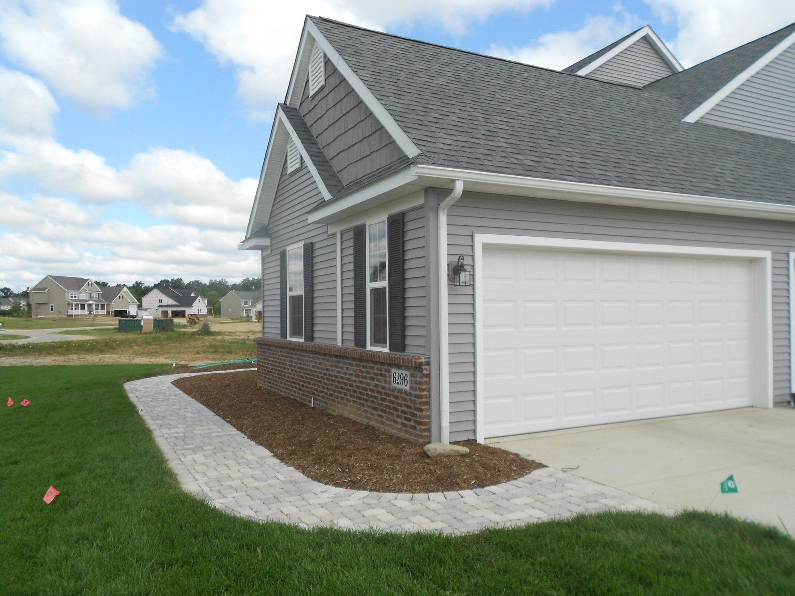 Suburban house exterior with gray siding, white garage, and curved concrete walkway beside a green lawn