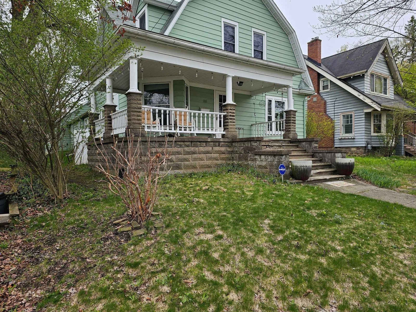 Mint-green house with white porch and stone steps, viewed from a front lawn under cloudy skies
