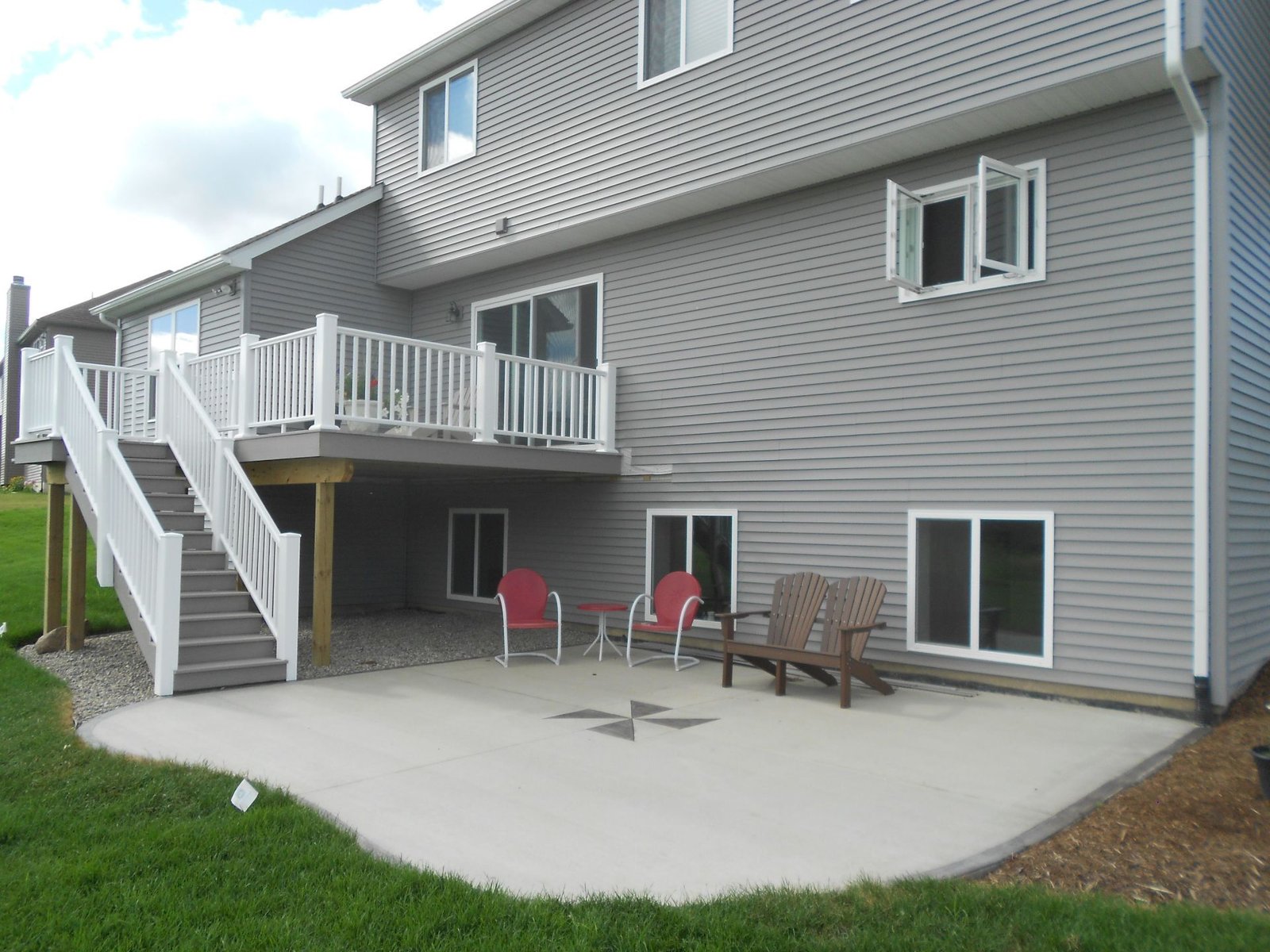 Back patio with white stairs, sliding doors, patio chairs, and a concrete seating area beside a gray house