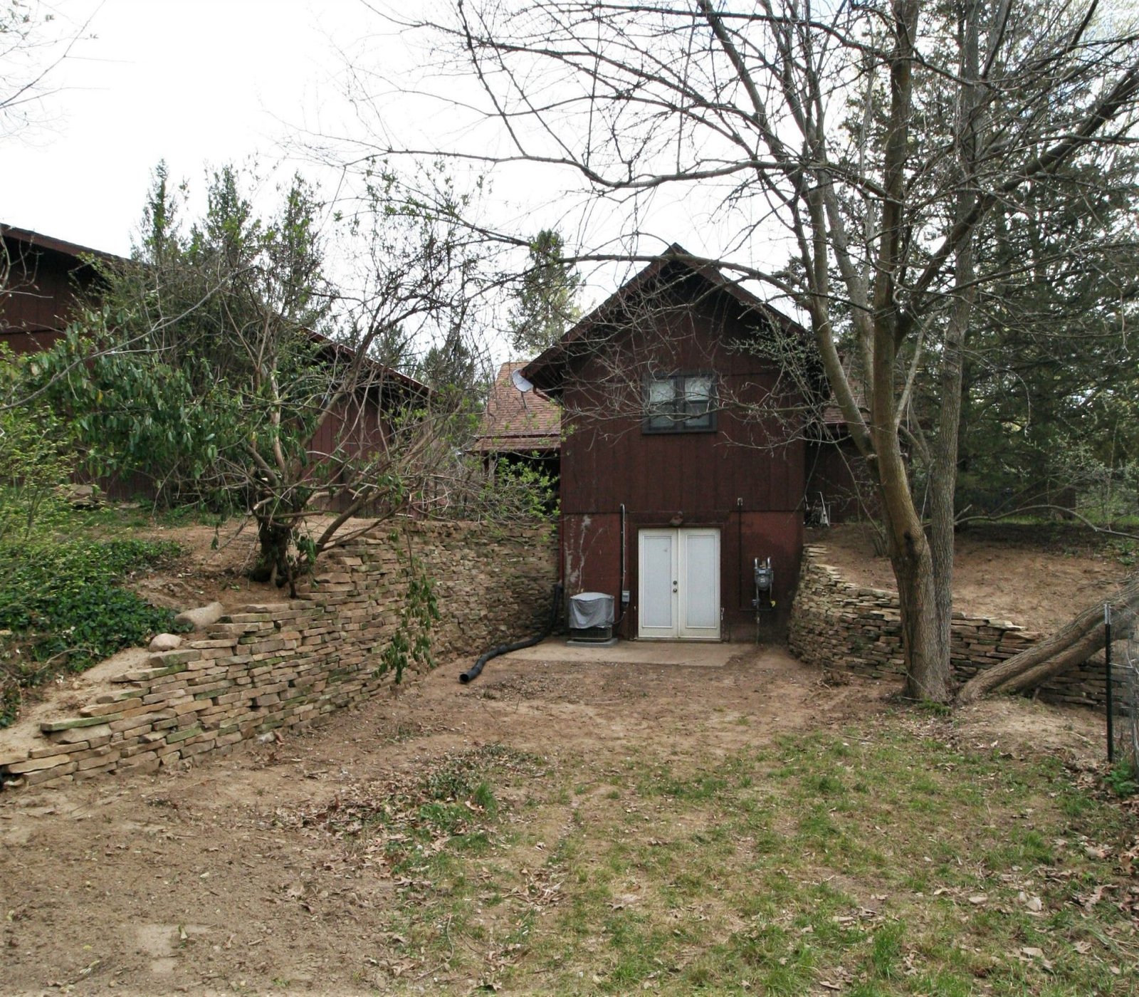 Backyard with curved dry-stack stone retaining walls leading to a brown barn-style outbuilding