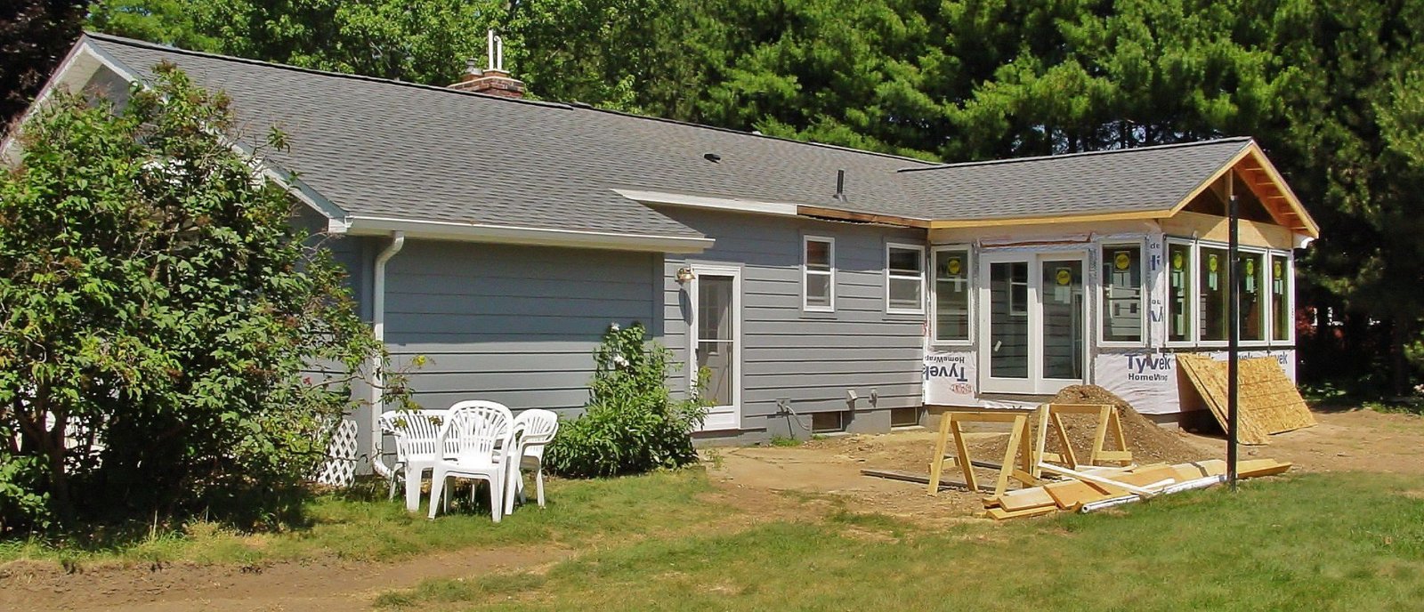 Gray house with a covered porch, white patio chairs, and a stone wall in a grassy yard
