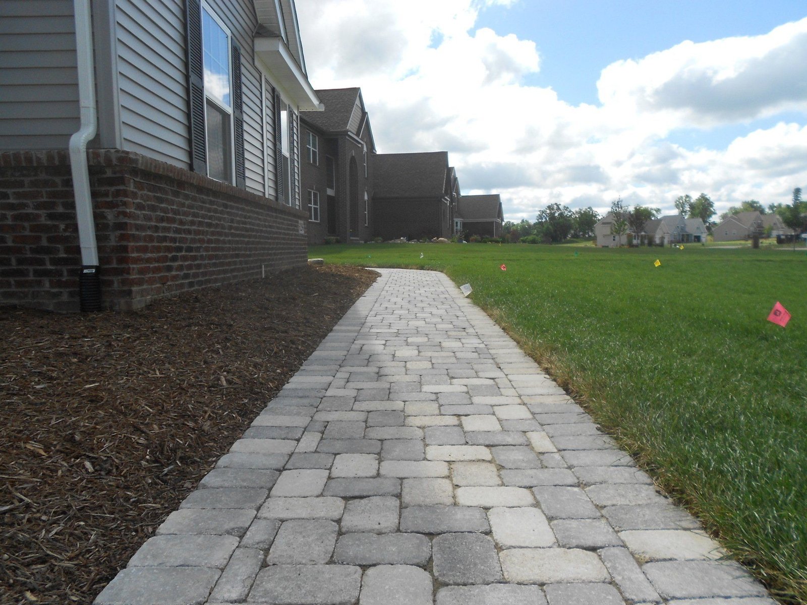 Paver walkway running along the side of a brick home through an open lawn