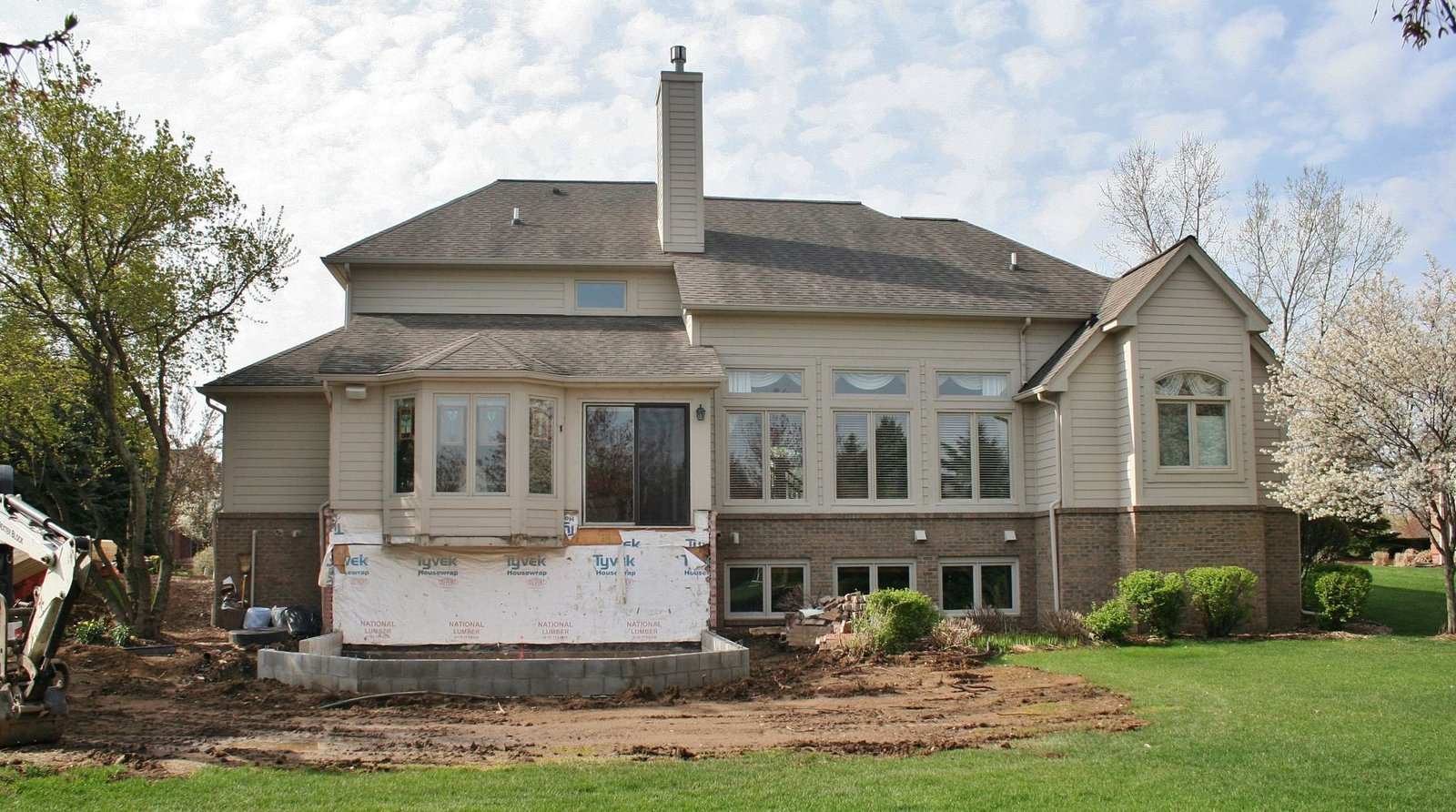 Single-story house exterior with white trim, large windows, and a front lawn and garden beds