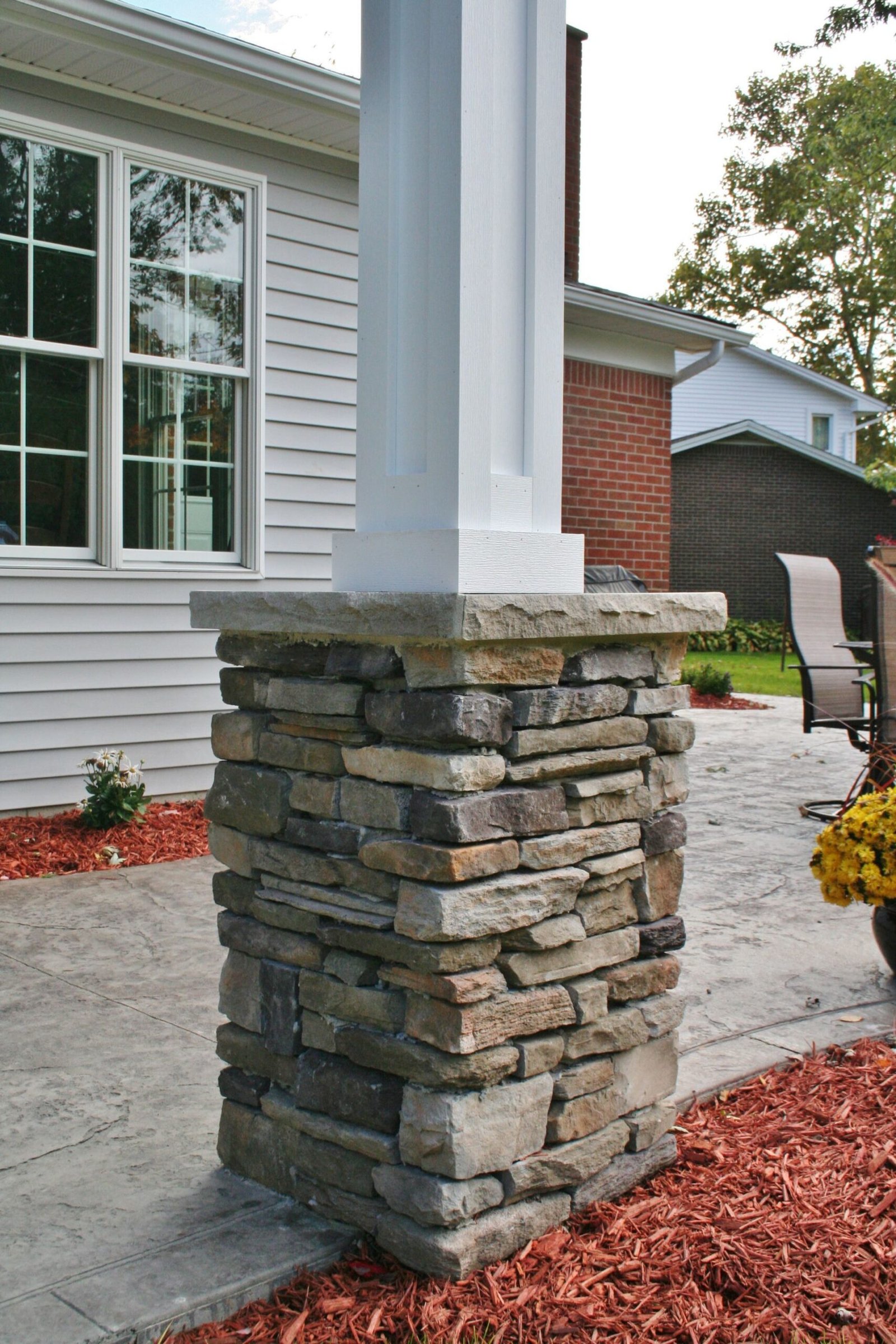 Stone-clad porch column beside a white house exterior with brick accent wall and concrete walkway