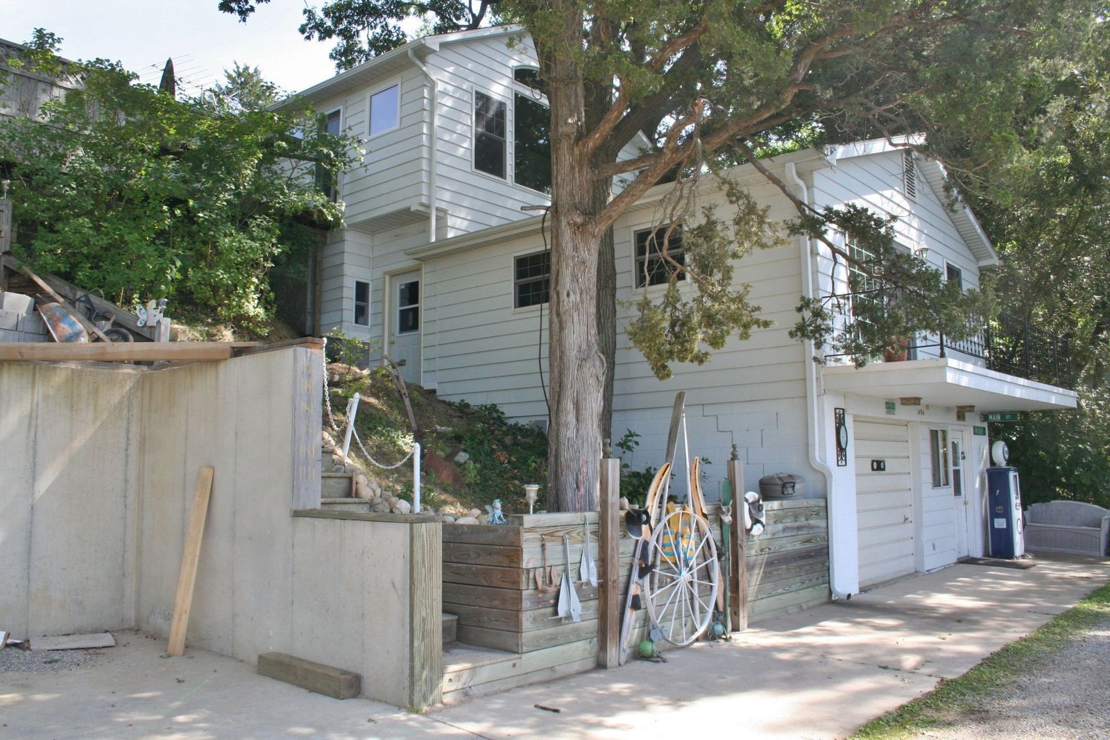 Residential hillside house with a tree, retaining wall, and garage under a bright sky