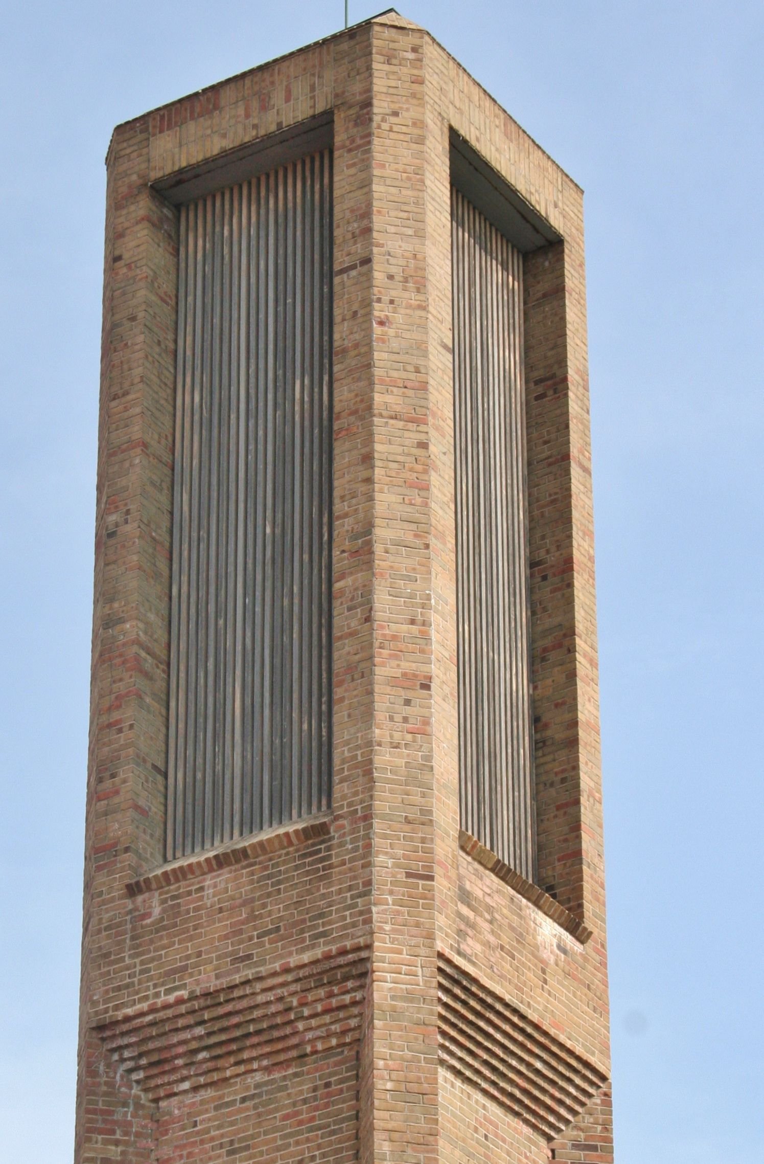 Tall brick tower with vertical metal louvers against a blue sky