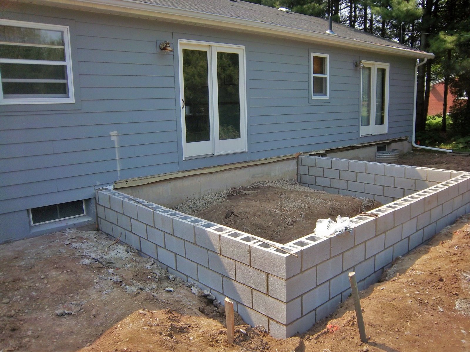 Backyard construction site with a new cinder block foundation beside a gray house