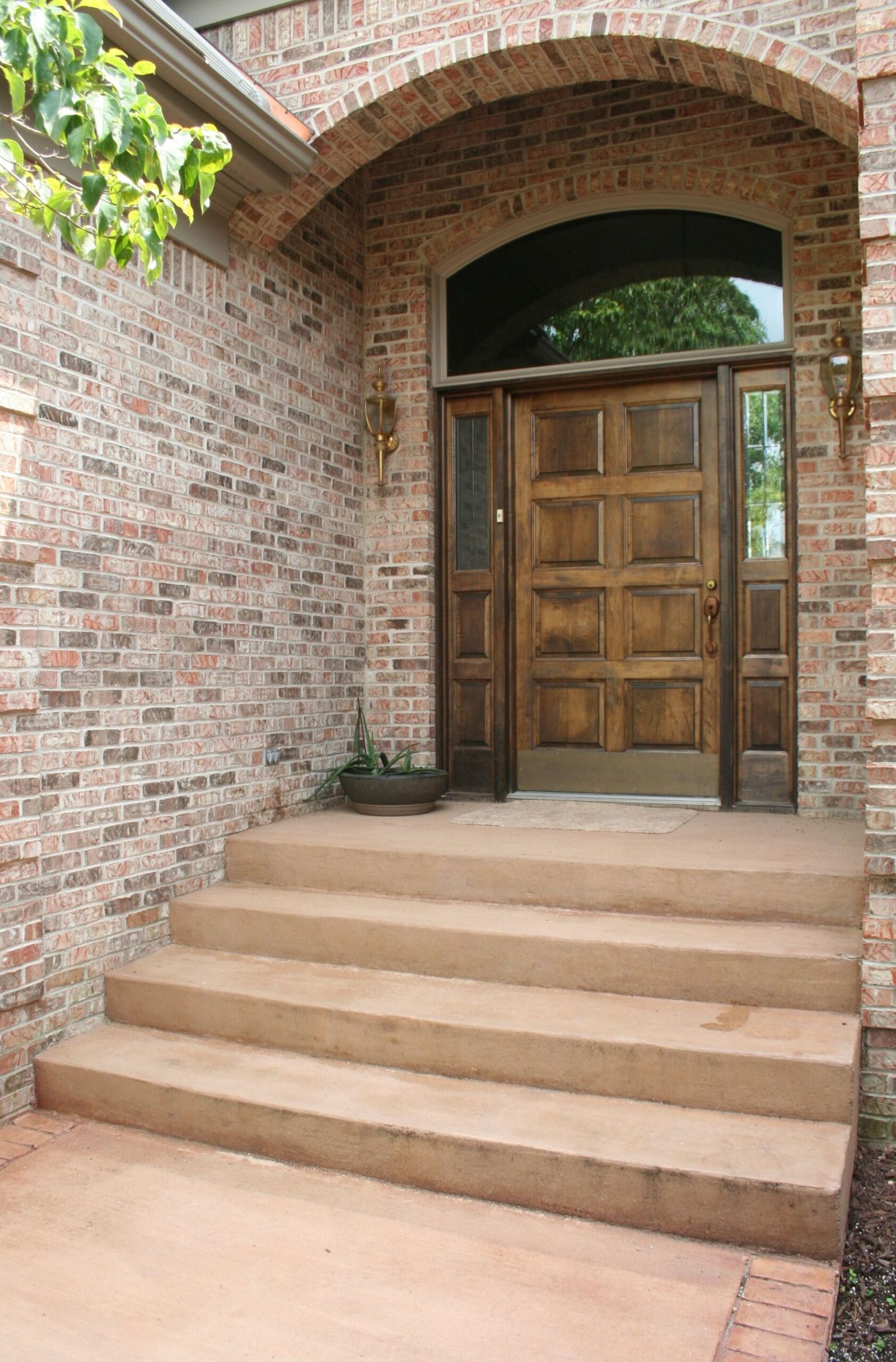 Brick entryway with steps leading to a wooden double door under an arched brick archway