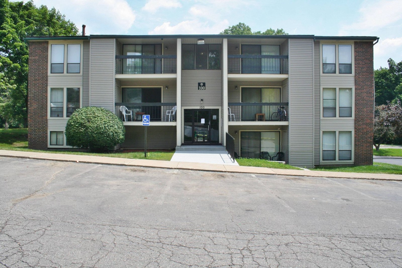 Apartment building exterior with balconies, brick sides, and a central entrance facing an empty parking lot