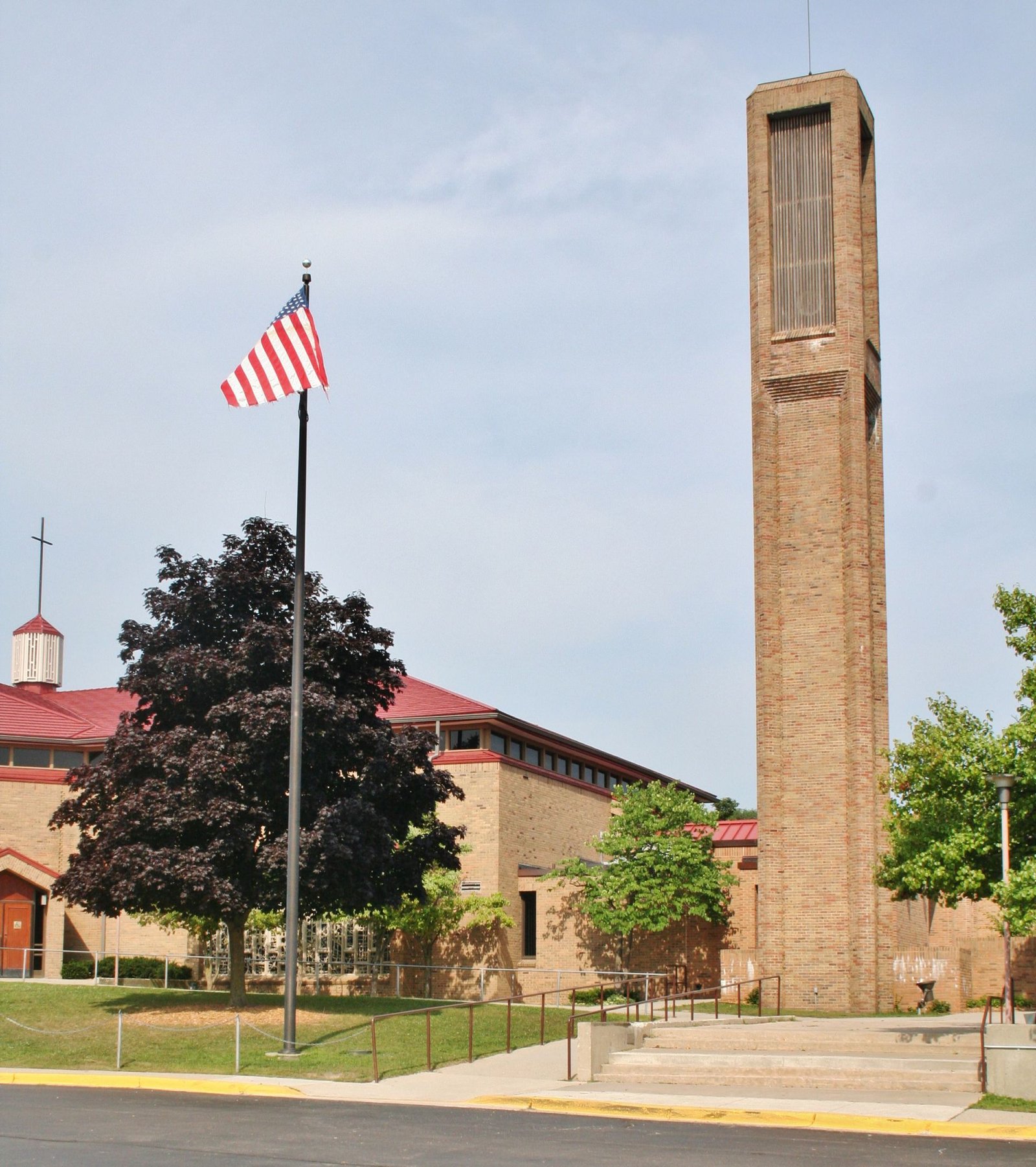 Brick clock tower beside a building, with an American flag in front on a sunny day.
