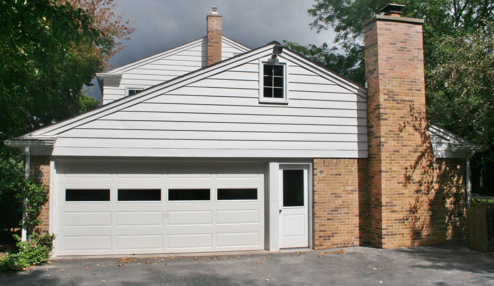 Suburban house with white siding, two-car garage, and tall brick chimney under a cloudy sky