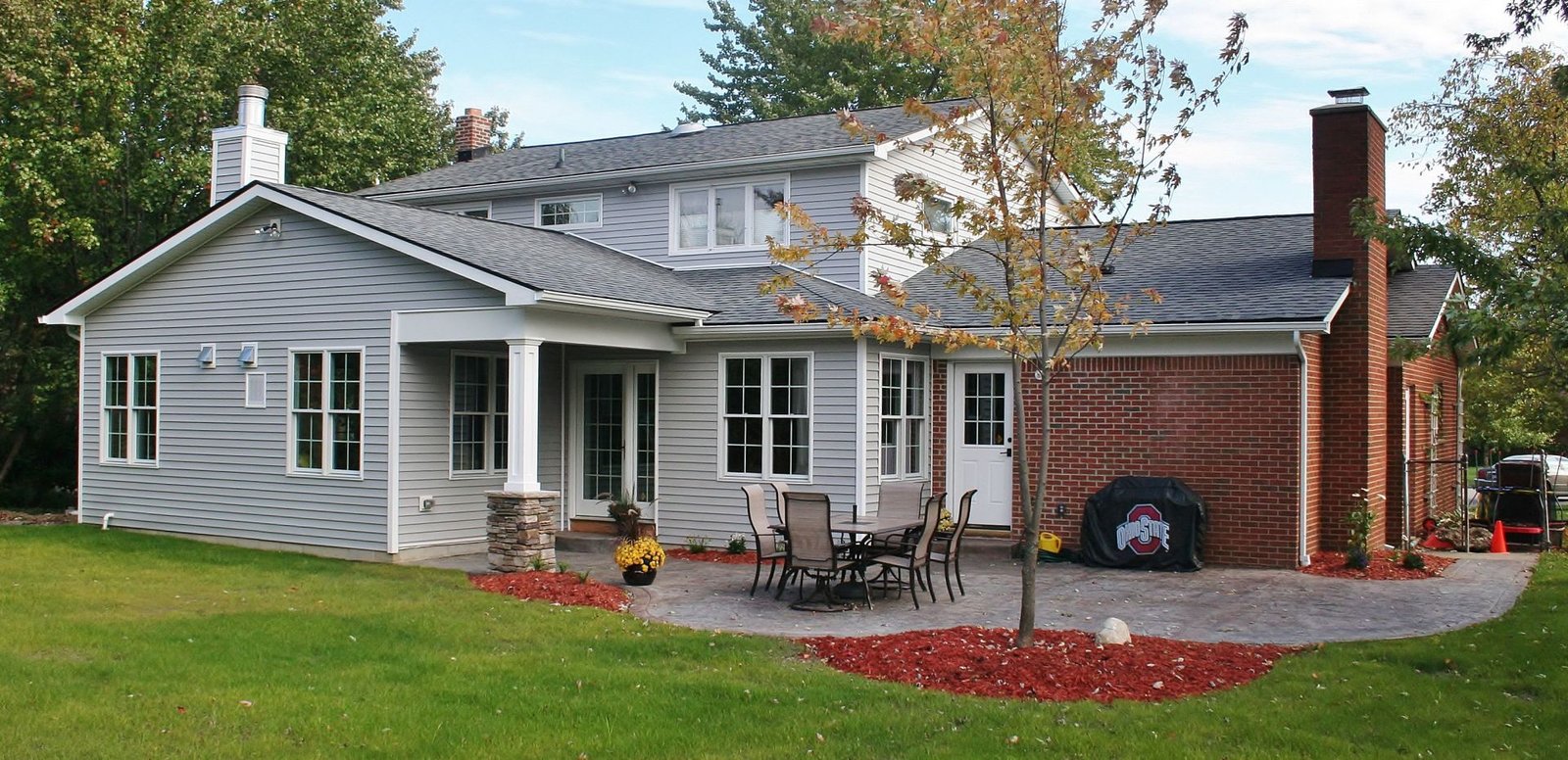 White single-story house with porch, brick chimney, and patio set in a green yard with autumn leaves.
