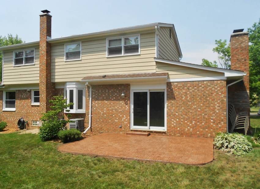 Two-story brick house with tan siding, brick patio, and green lawn in front