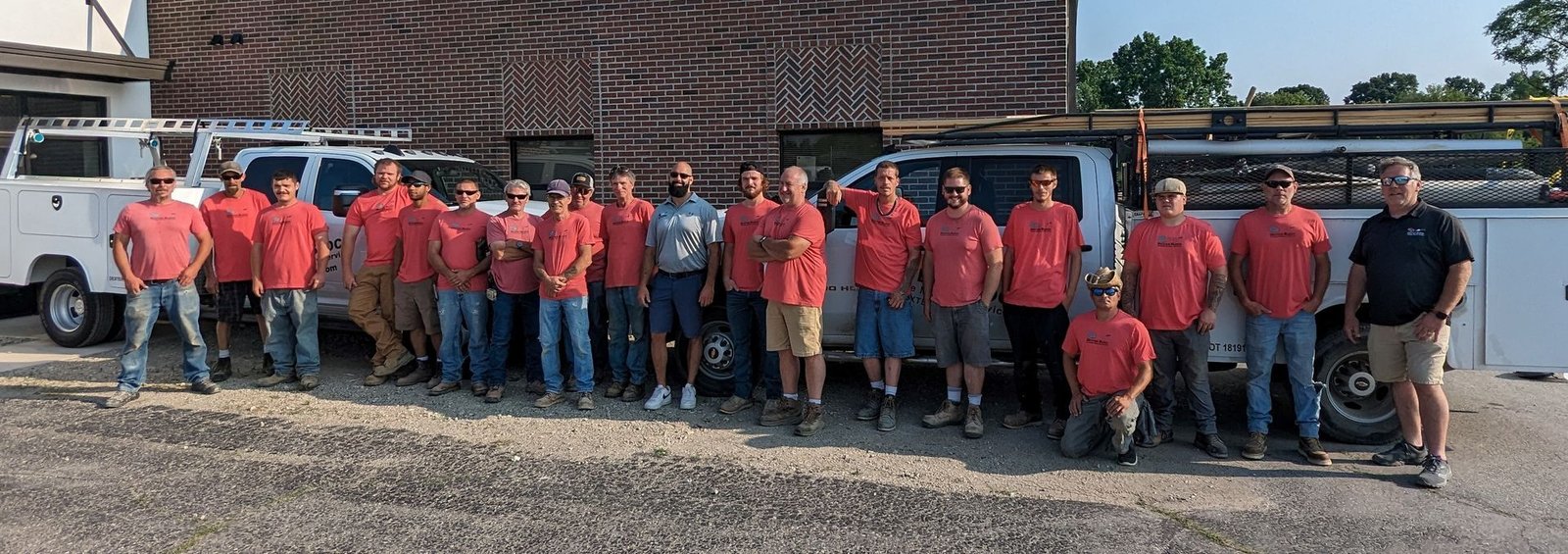 Group of workers in red shirts standing beside a truck and large industrial equipment outdoors