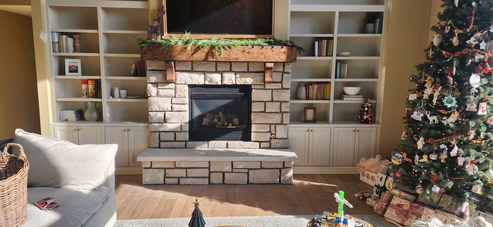 Cozy living room with a stone fireplace, built-in shelves, and a decorated Christmas tree on the right
