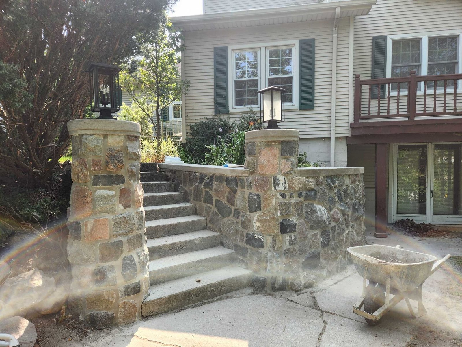 Stone staircase with railings leading to a house entrance and patio in a yard.
