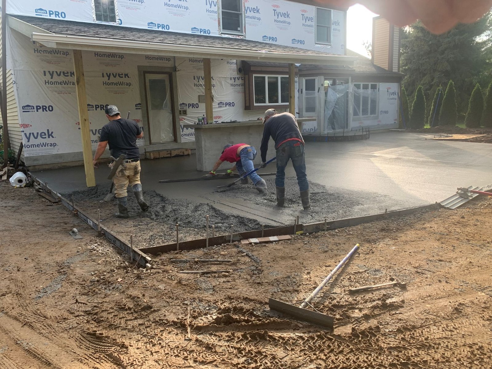 Workers spread wet concrete outside a storefront, leveling a sidewalk in front of shops.