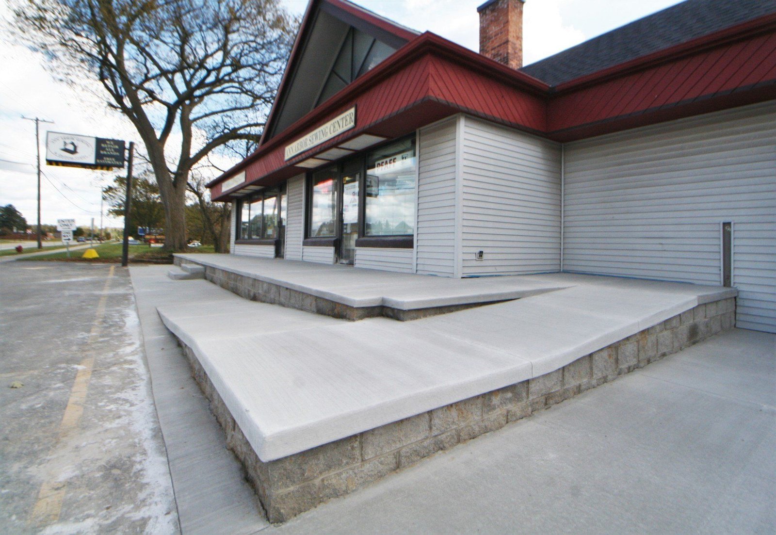 Exterior of a commercial building with a large concrete ramp and steps, under a red-trimmed roof