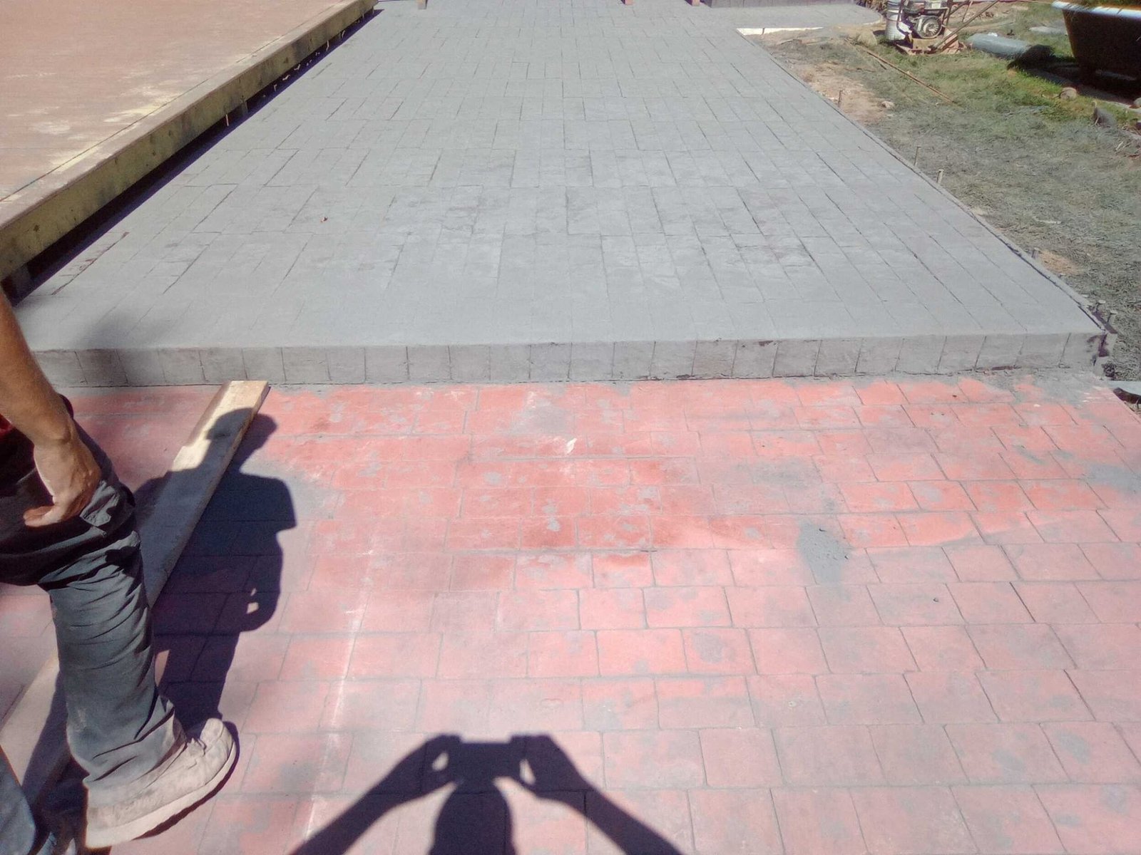 Brick walkway leading to a concrete path, with a person’s leg visible at left and a shadow in the foreground