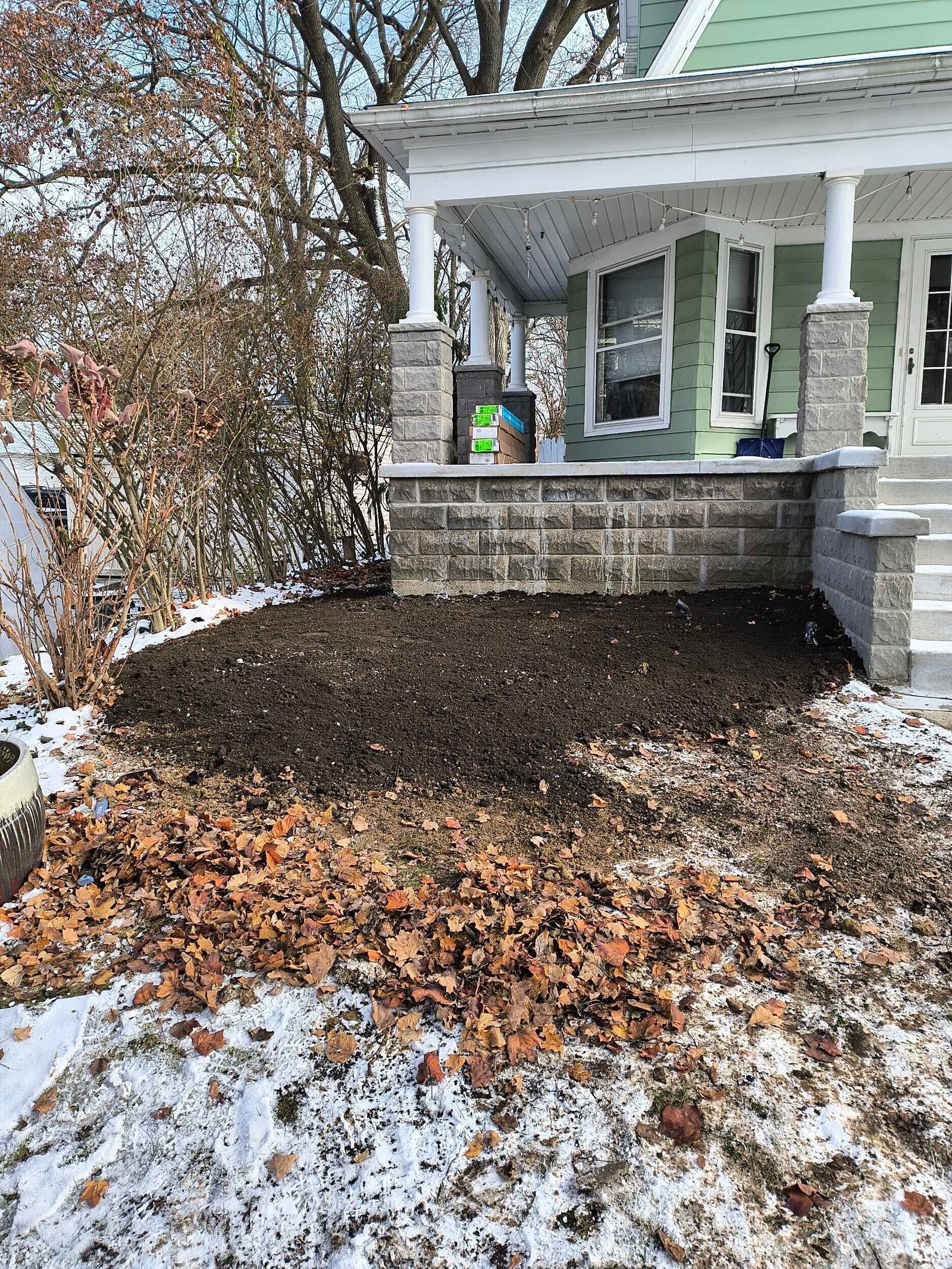 Snowy front yard with a house porch, leaf pile, and a child’s toy near the steps