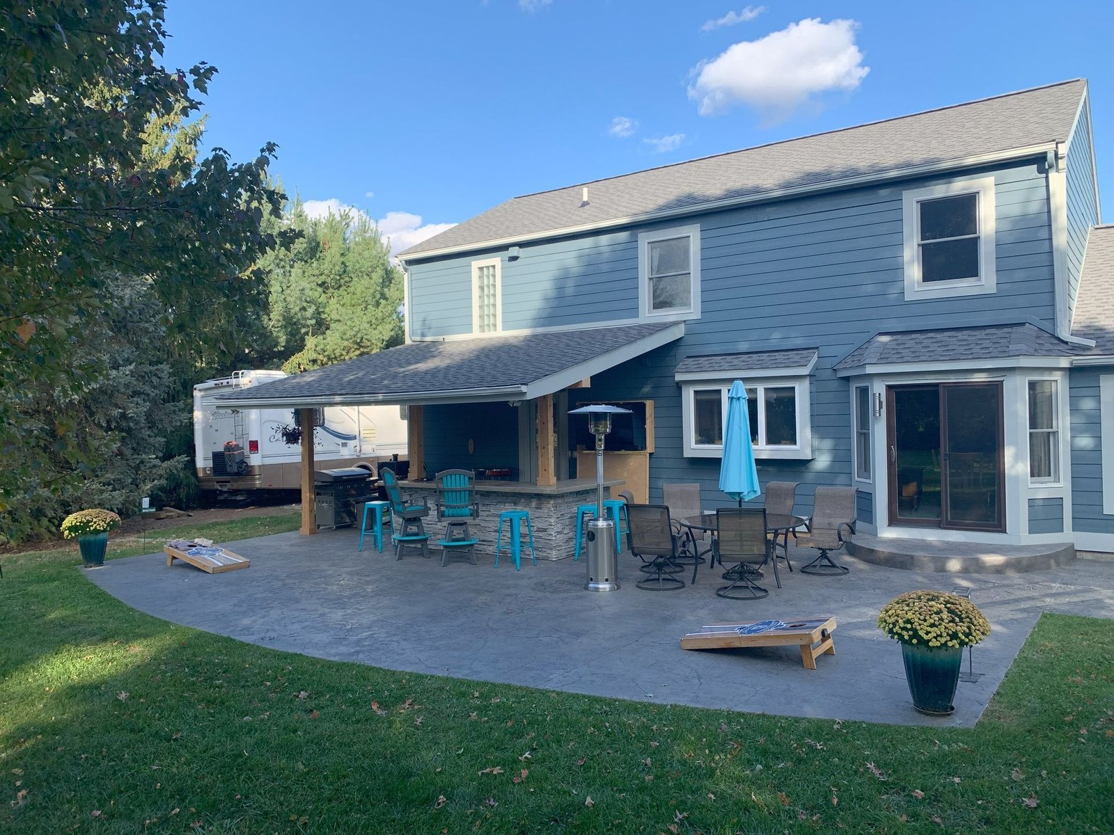 Backyard patio with two-story gray house, covered seating area, and lawn in the foreground