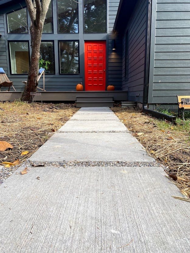 Front walkway leading to a house with a bright red front door and a pumpkin by the steps.