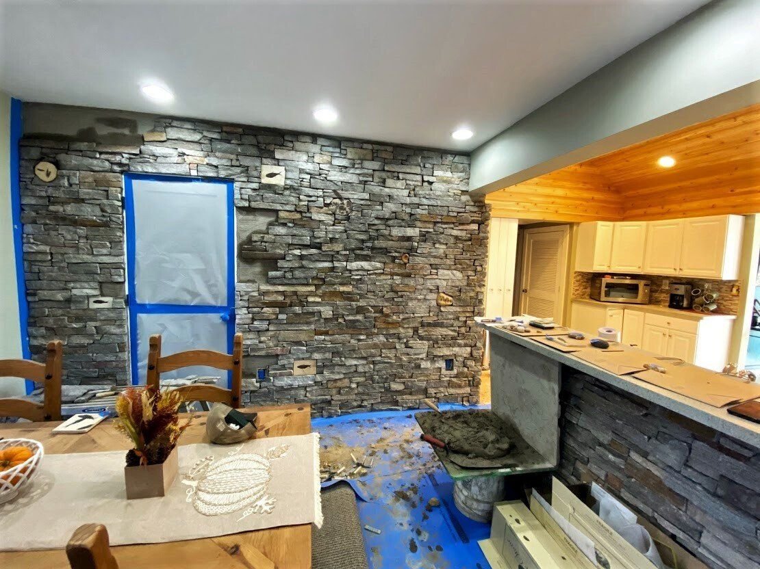 Stone-walled kitchen and dining area with blue floor covering and wood-paneled pass-through counter