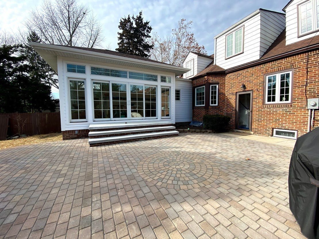 Paver patio beside a white sunroom and brick house