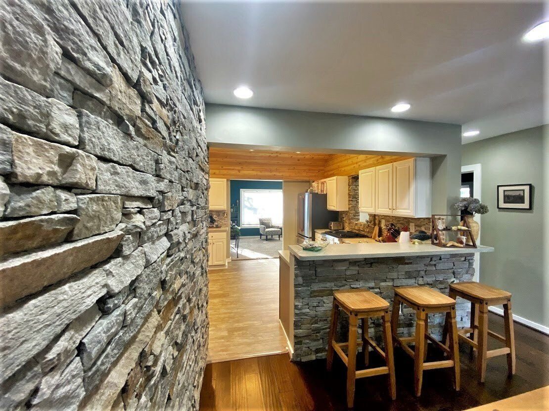 Modern kitchen with stone accent wall, wooden island, and three stools in an open, warmly lit home interior