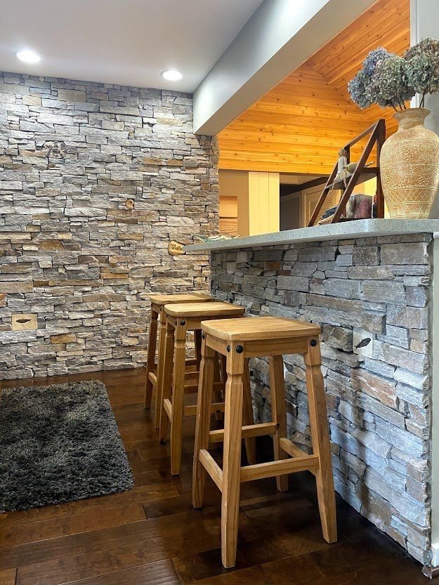 Stone-and-wood bar with stools in a rustic interior, featuring a stacked-stone wall and warm wood accents