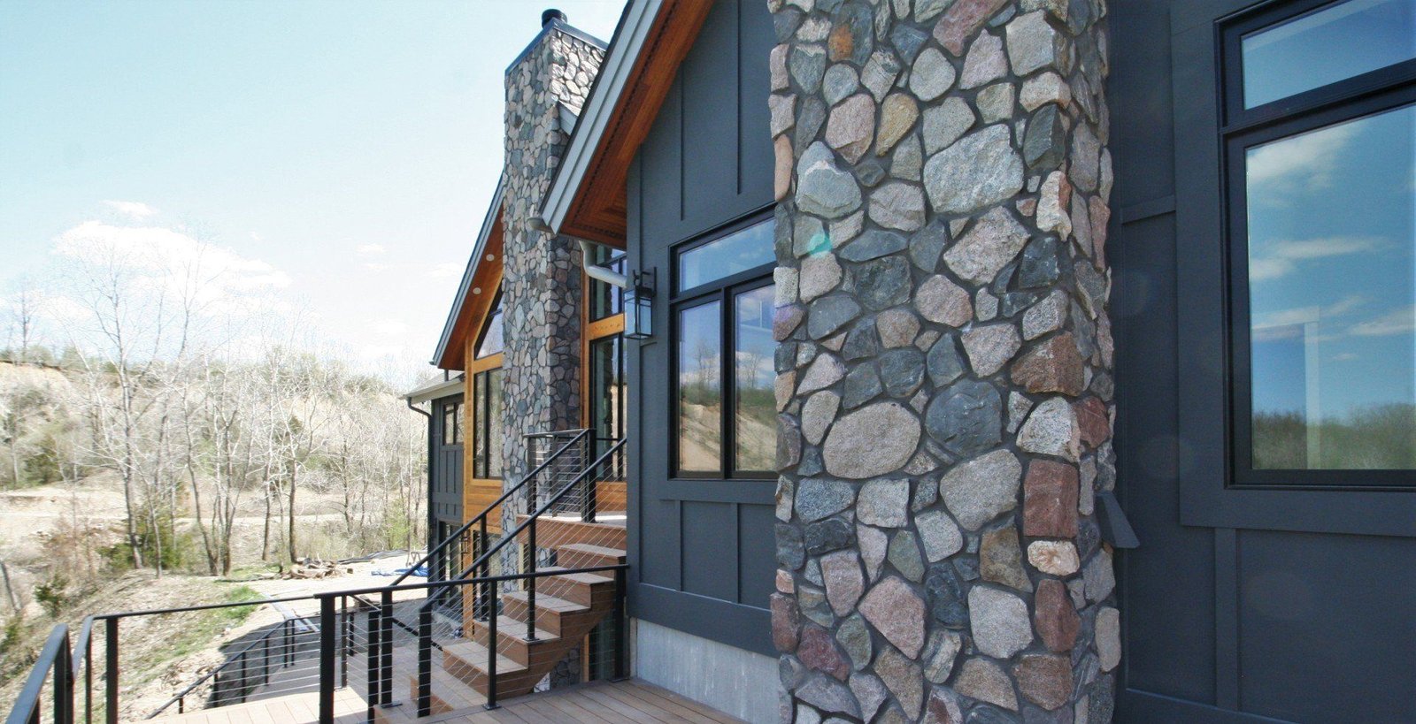 Modern stone-and-dark-siding house exterior with large windows and a front porch overlooking a hillside