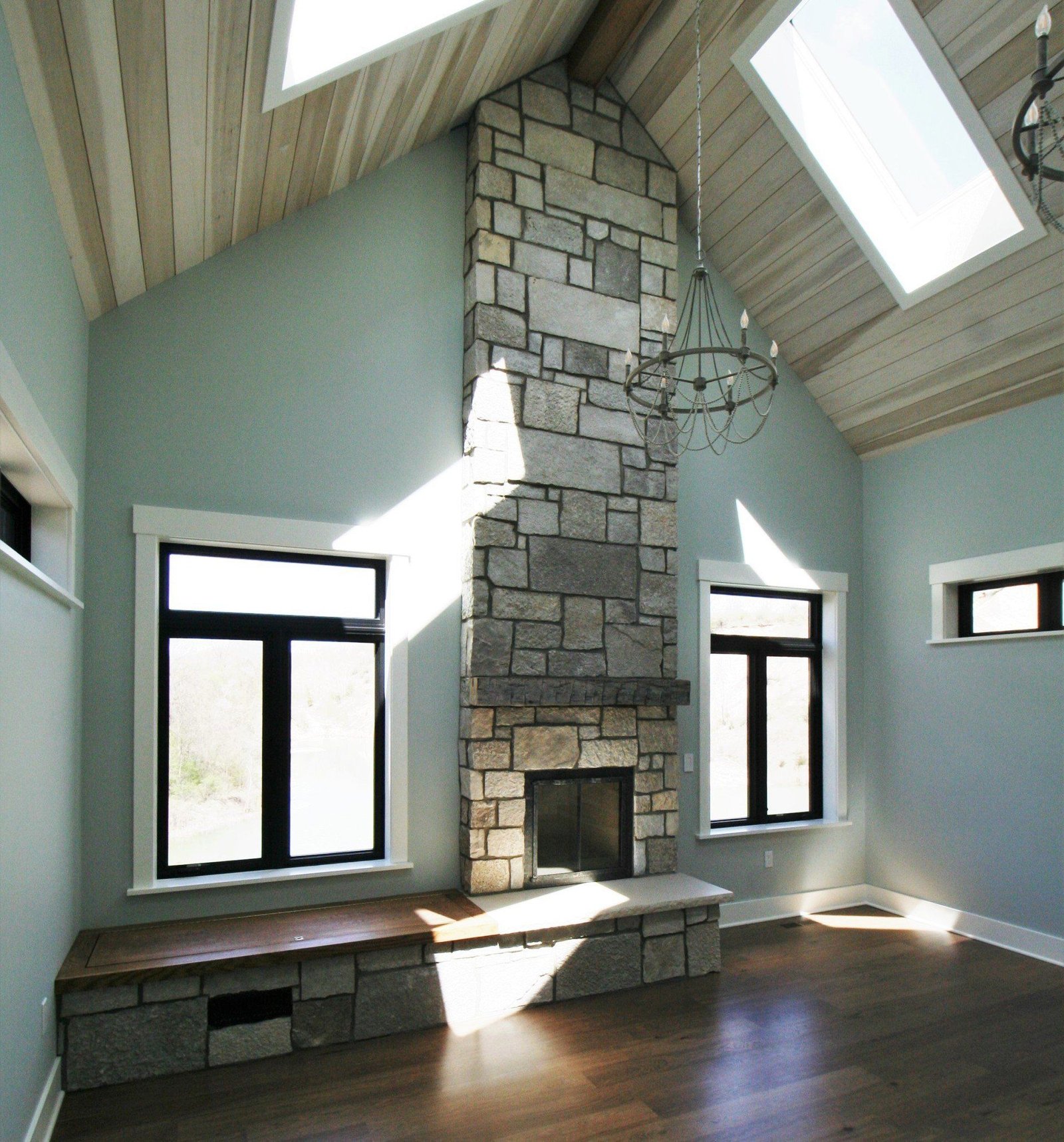 Bright vaulted room with skylights, stone fireplace, and large windows over dark hardwood floors