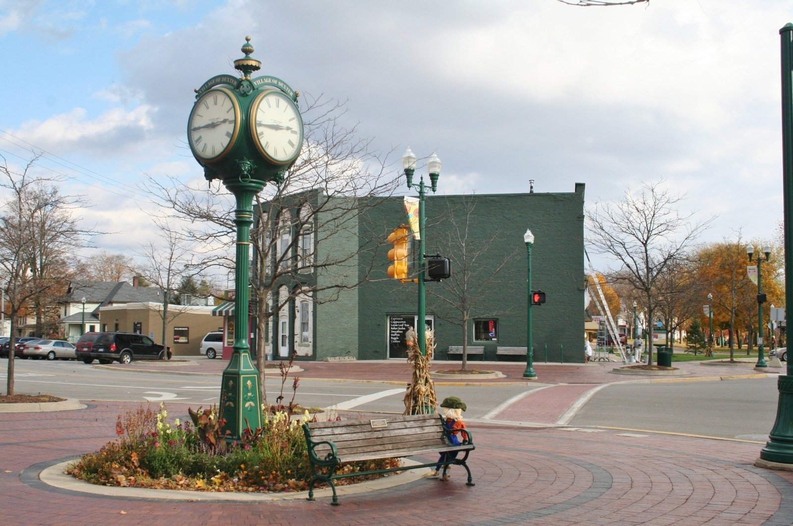 Town square with a green clock tower, traffic lights, and a child on a bench near a brick roundabout
