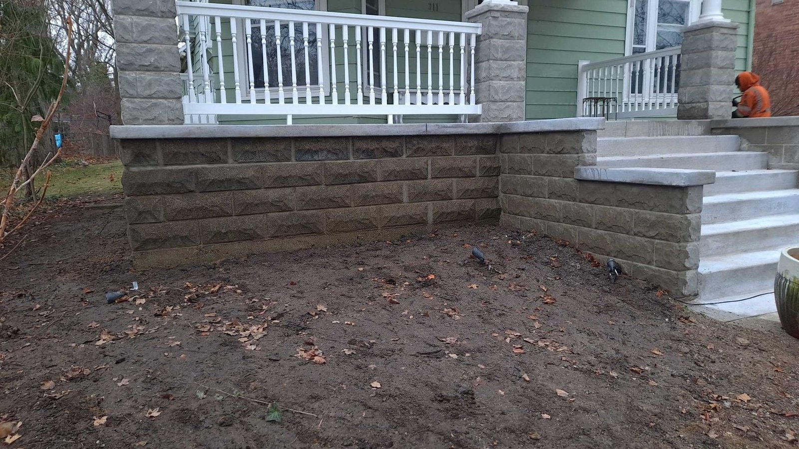 Front steps and stone retaining wall leading to a white porch, with bare dirt yard in front