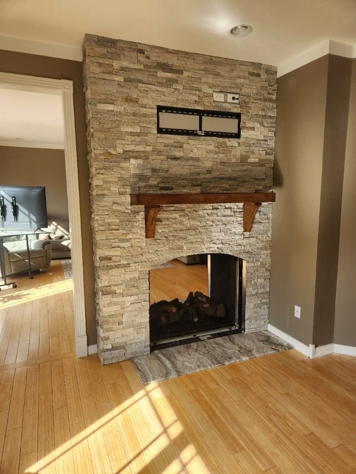 Living room with stone fireplace, wooden mantel, and sunlight on hardwood floor