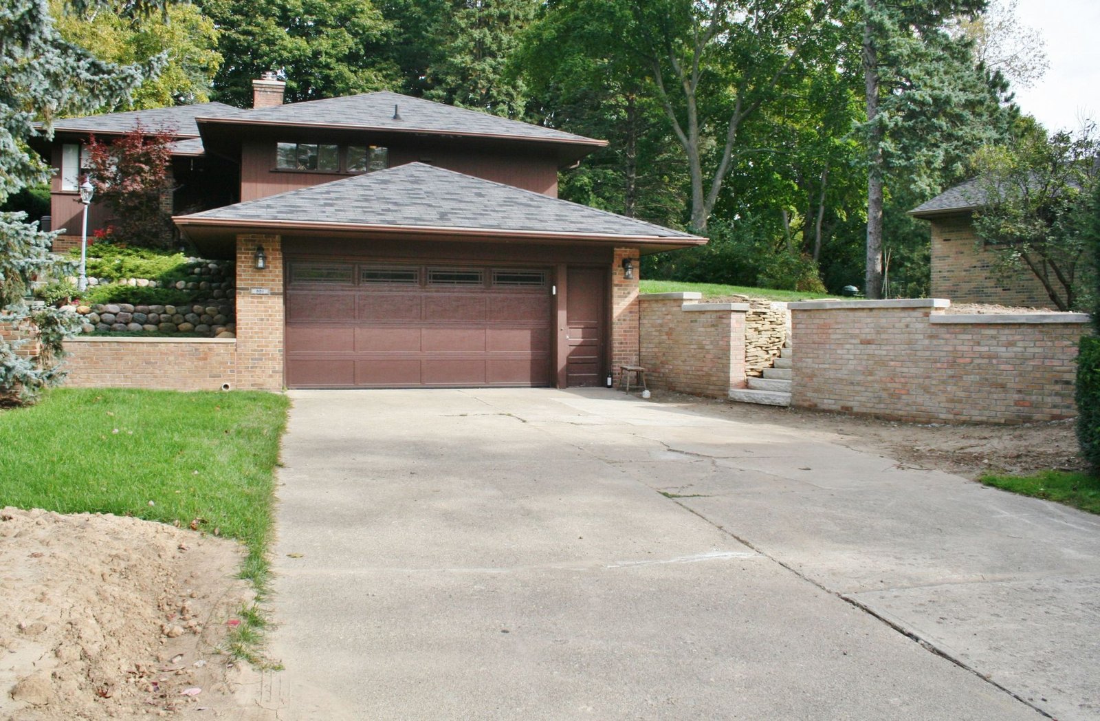 Modern brick house with a double garage, stone wall, and sloped driveway surrounded by trees