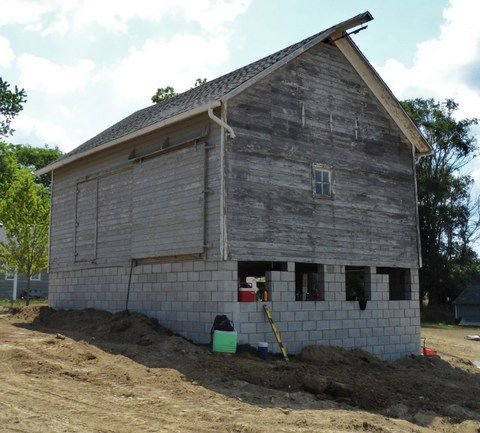 Unfinished wooden house with gray cinder block foundation on a dirt lot.