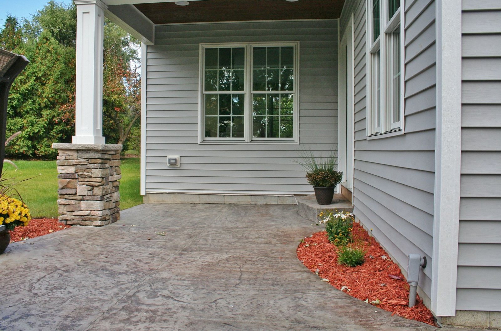 Stamped concrete patio corner with stone-veneer porch column against gray vinyl-sided home