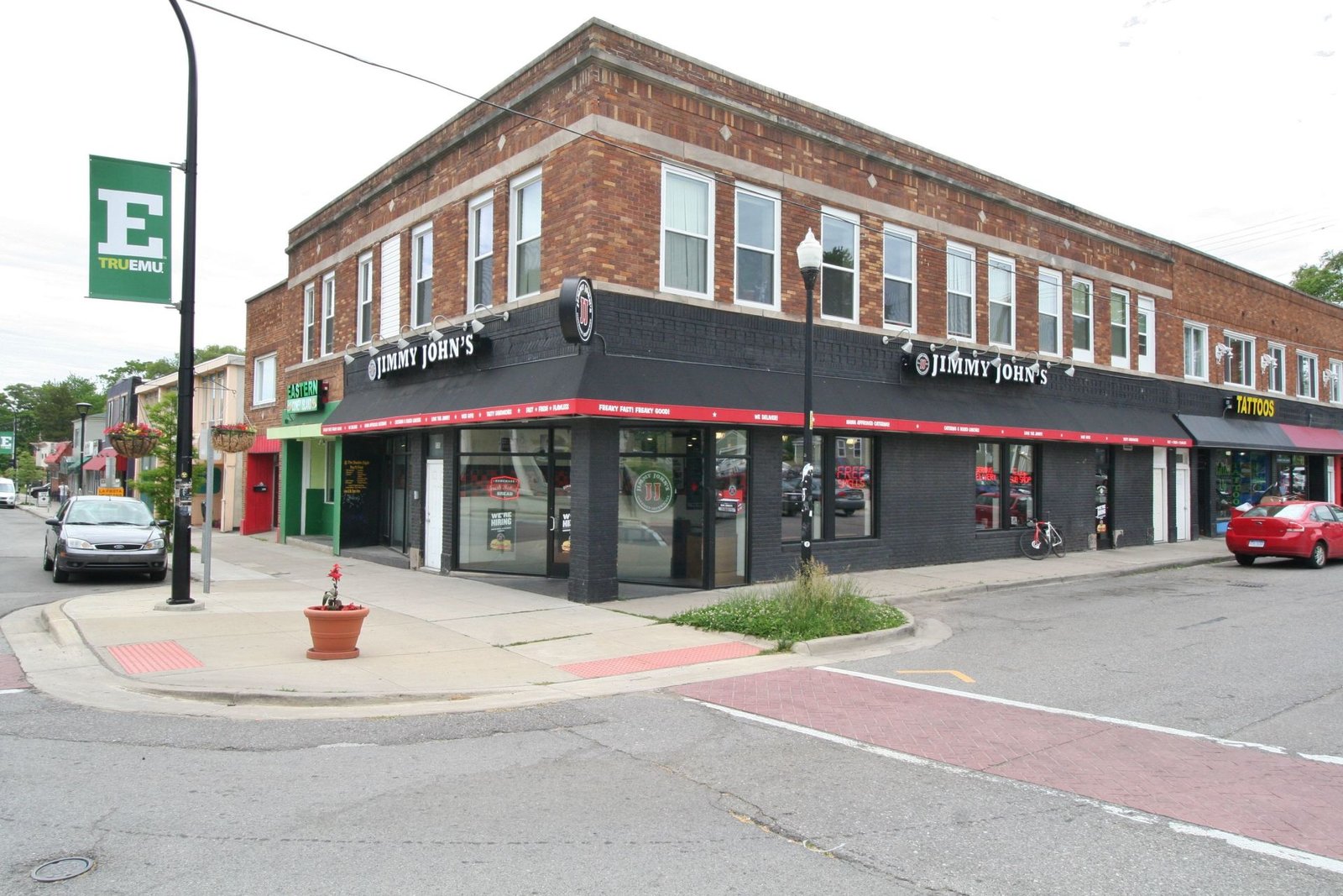 Corner brick storefront with black awning and red trim on a city street corner