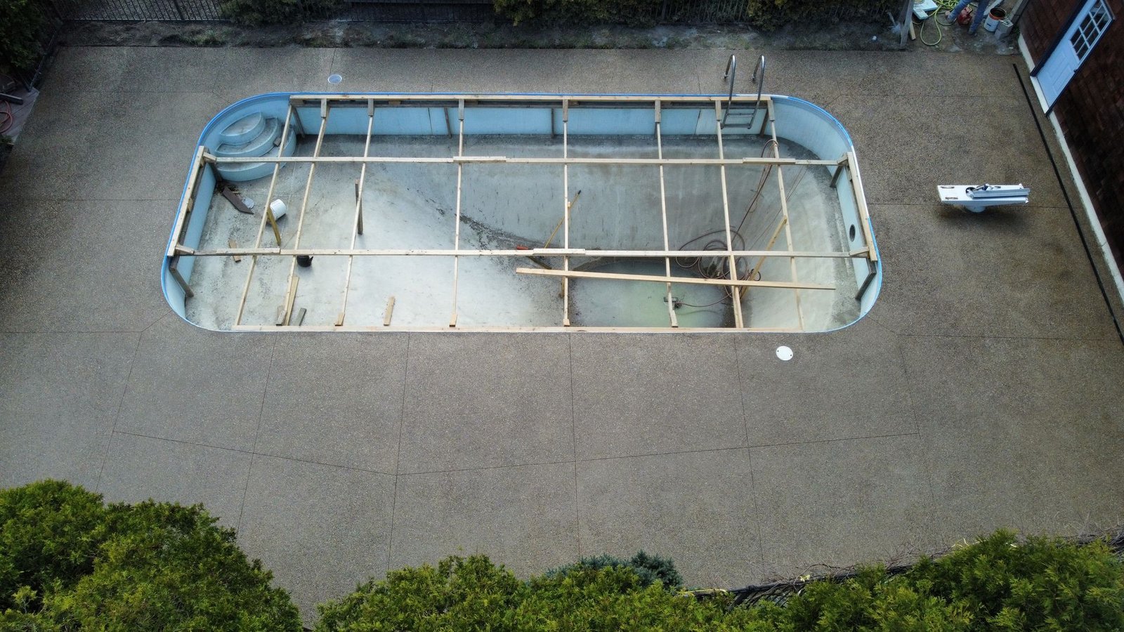 Empty swimming pool under maintenance, with exposed metal framing and surrounding concrete deck