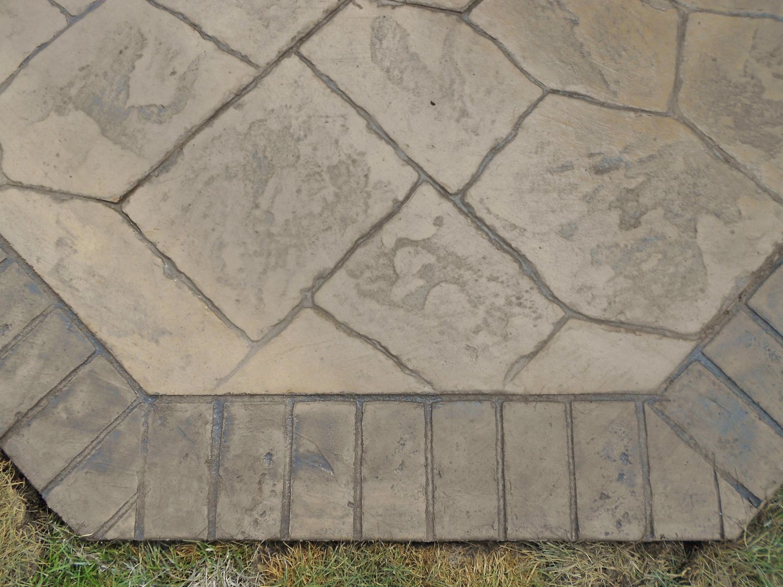 Stone walkway with irregular tan pavers and a gray border beside grass